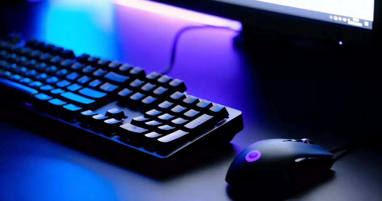 Gaming keyboard and mouse lit by monitor glow on a dark desk