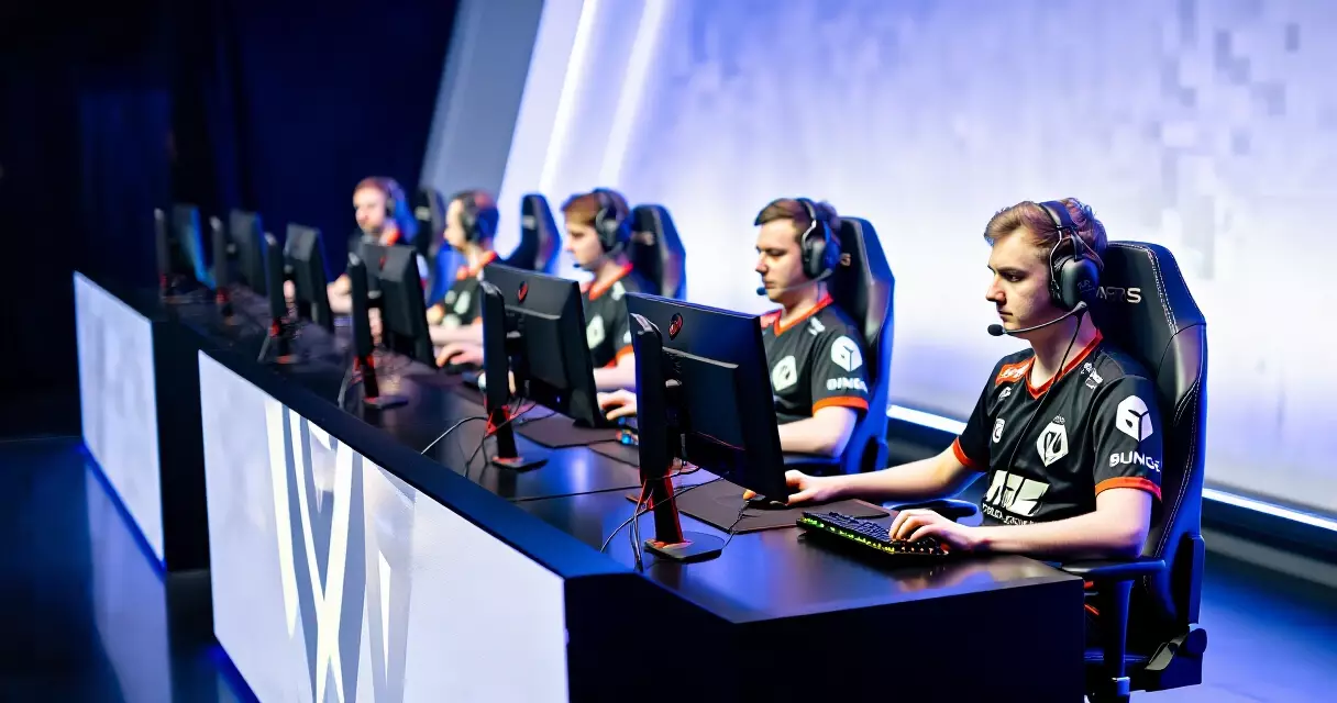 Esports team players seated at competition stations wearing branded jerseys in a tournament arena