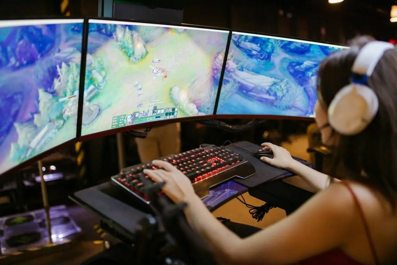 A young woman intently gaming on a multi-screen setup, showcasing vibrant gaming visuals.